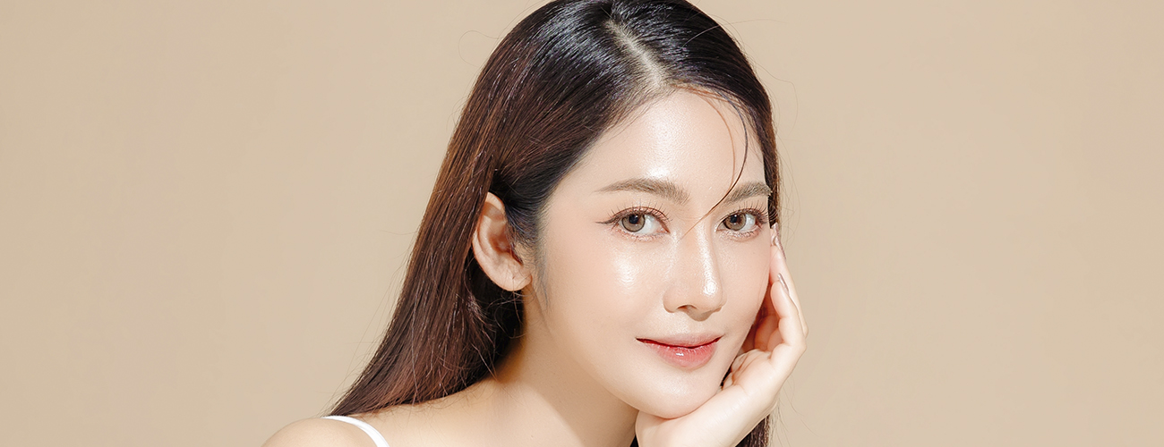 A portrait of a smiling young Asian woman, dressed in a white tank top against a neutral background.