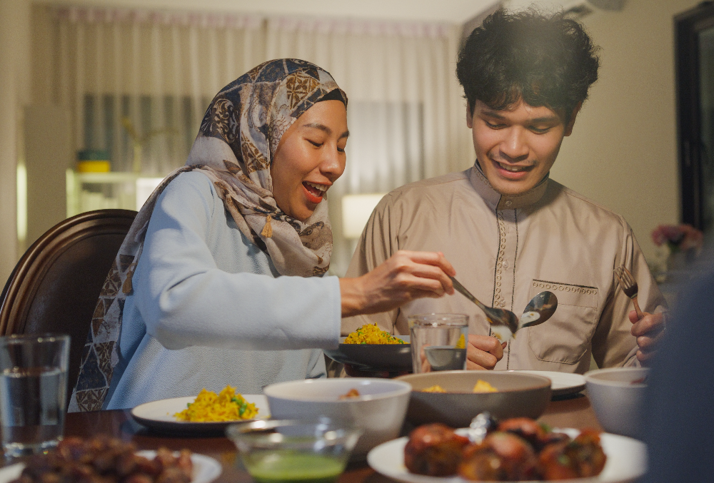 A hijabi lady serving food for a man.