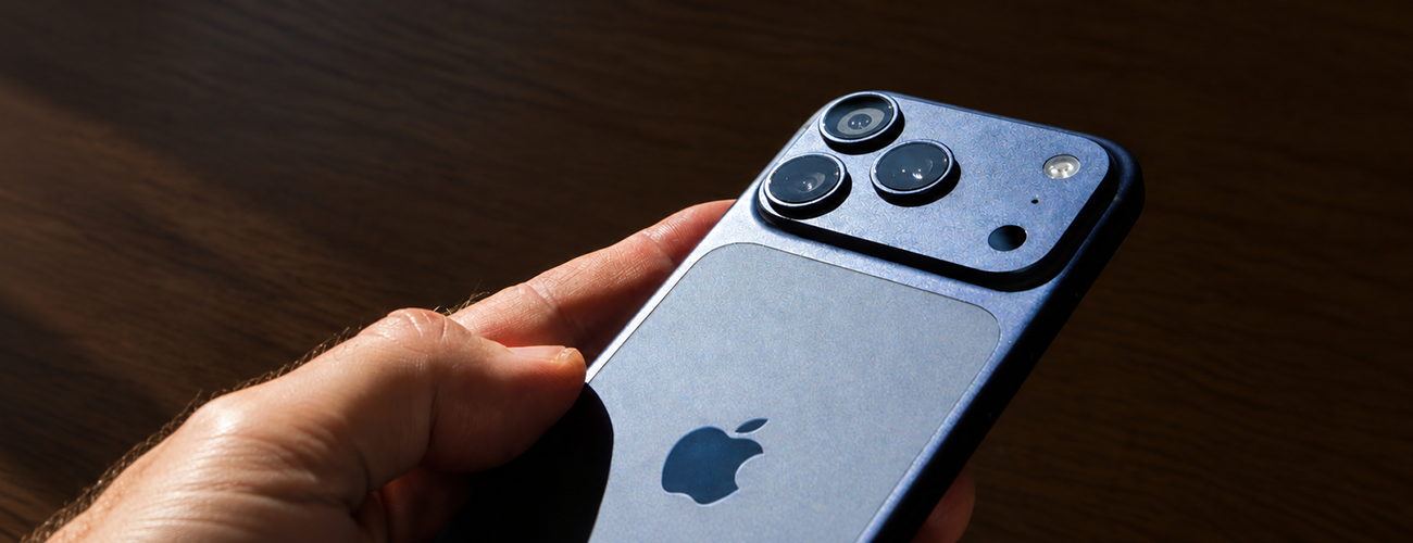 Hand holding iPhone 18 in a blue finish, showing its triple-lens rear camera.